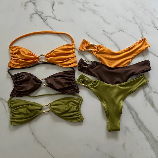Set of orange, brown, and green bikini pieces on a marble surface