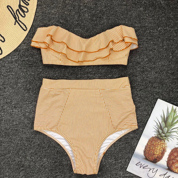 Two-piece swimsuit with ruffled top and high-waisted bottom on a textured surface with a pineapple-themed card.