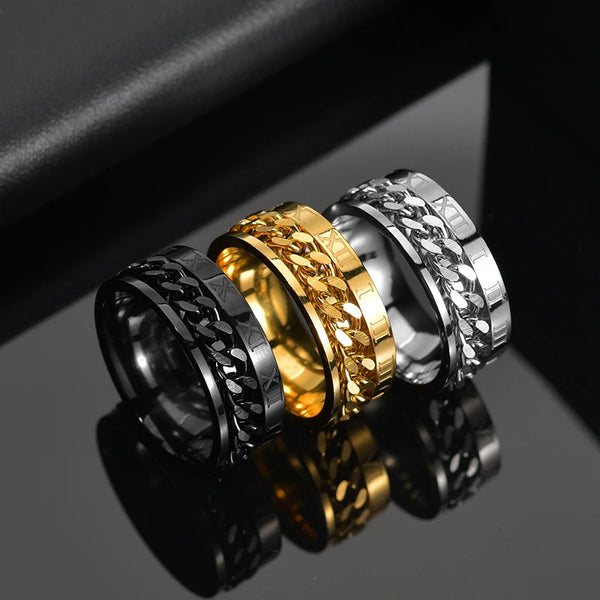 Three metallic rings in black, gold, and silver on a reflective surface.