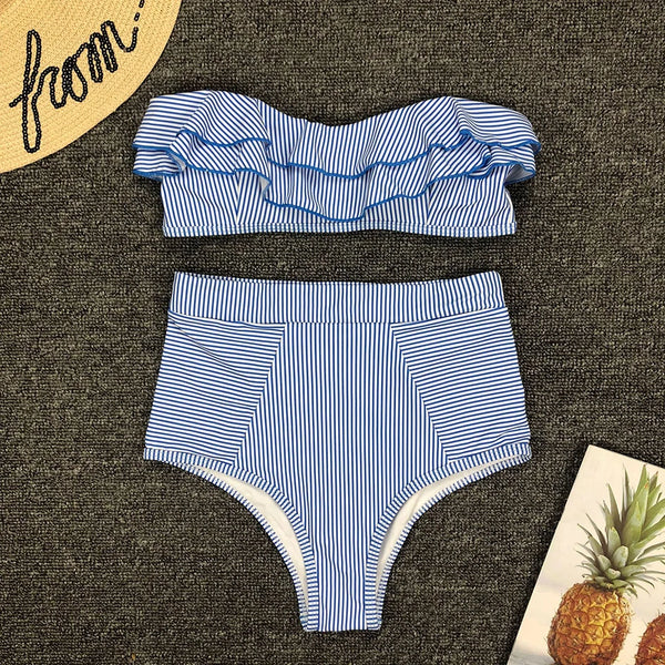 Blue and white striped bikini set on a textured surface with a straw hat and pineapple decorations.