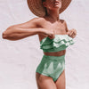 Woman wearing a green and white striped bikini with a straw hat on a light background