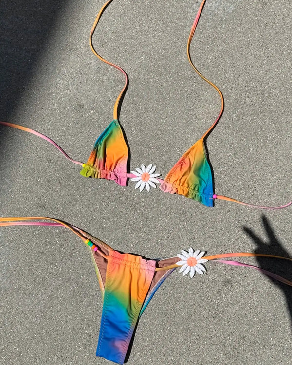 Rainbow tie-dye bikini set on a textured surface with flowers.