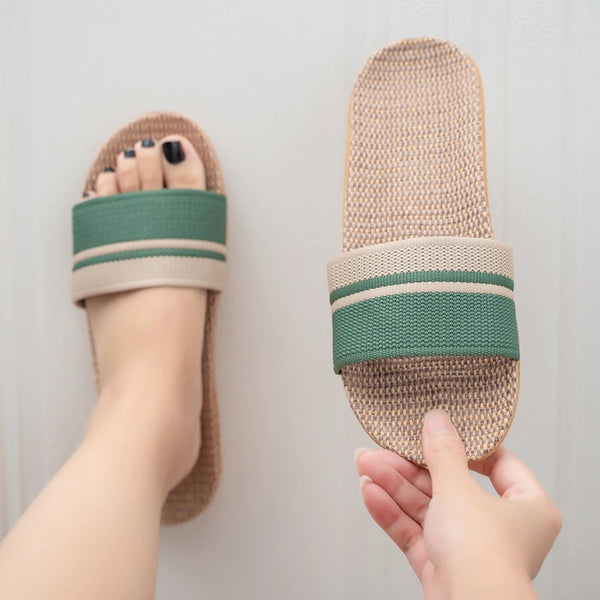 Pair of slippers with a green band held by a hand against a neutral background