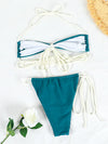 Teal and white bikini set on a light background with a flower and straw hat.