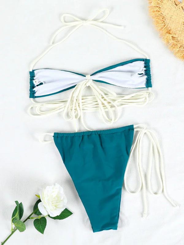 Teal and white bikini set on a light background with a flower and straw hat.