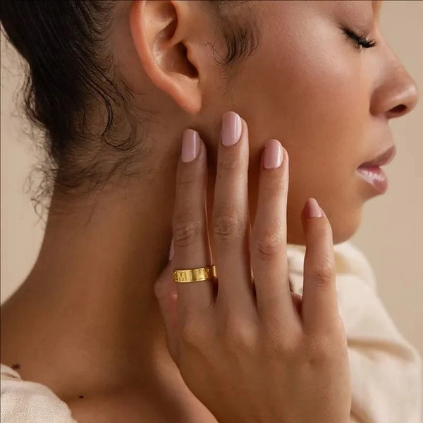 Close-up of a woman's hand with a gold ring on her finger, wearing pink nail polish.
