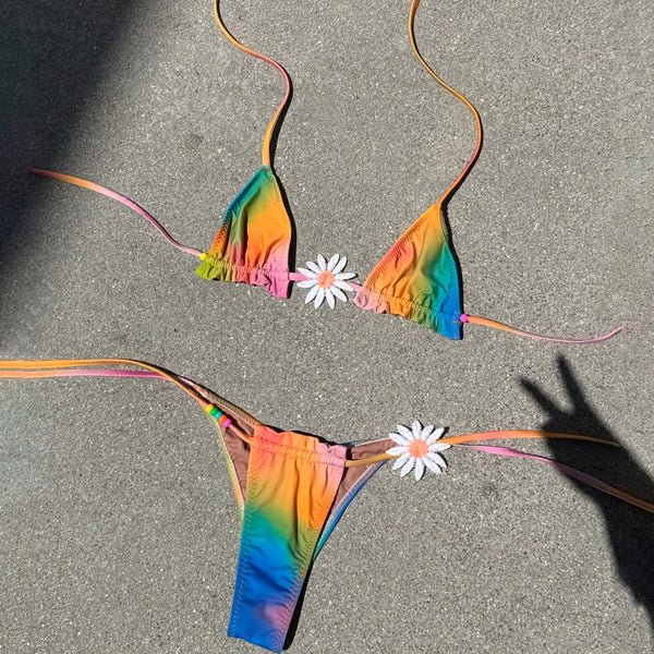 Colorful tie-dye bikini set on a sandy surface with flowers.