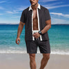 Man standing on a beach wearing a dark shirt and shorts with a white collar.