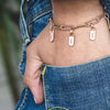 Rose gold chain bracelet with name tags worn on a wrist against a blurred denim background