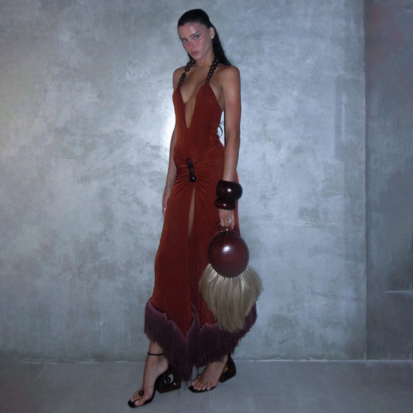 Woman in a long, dark red dress with feathered details against a gray background