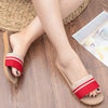 Red and beige sandals worn on a wooden floor with a woven mat in the background.