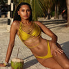 Woman in a yellow bikini sitting on a beach with a coconut drink.