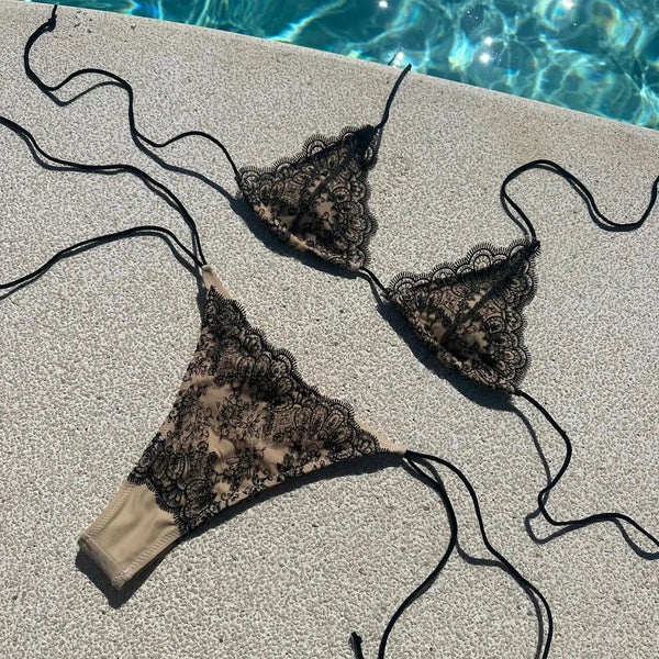 Black lace bikini set on a concrete surface near a pool.