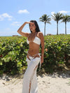 Woman in a white bikini and cover-up standing on a beach with palm trees in the background