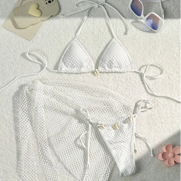 White bikini set on a textured surface with sunglasses and a phone in the background