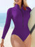 Person wearing a purple long-sleeve swimsuit with a zipper on a beach.