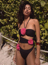 Woman wearing a black bikini with pink floral details against a natural background