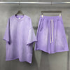 Purple t-shirt and shorts set hanging on a rack against a gray background