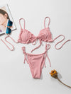 Pink bikini set on a white surface with a magazine and sunglasses.