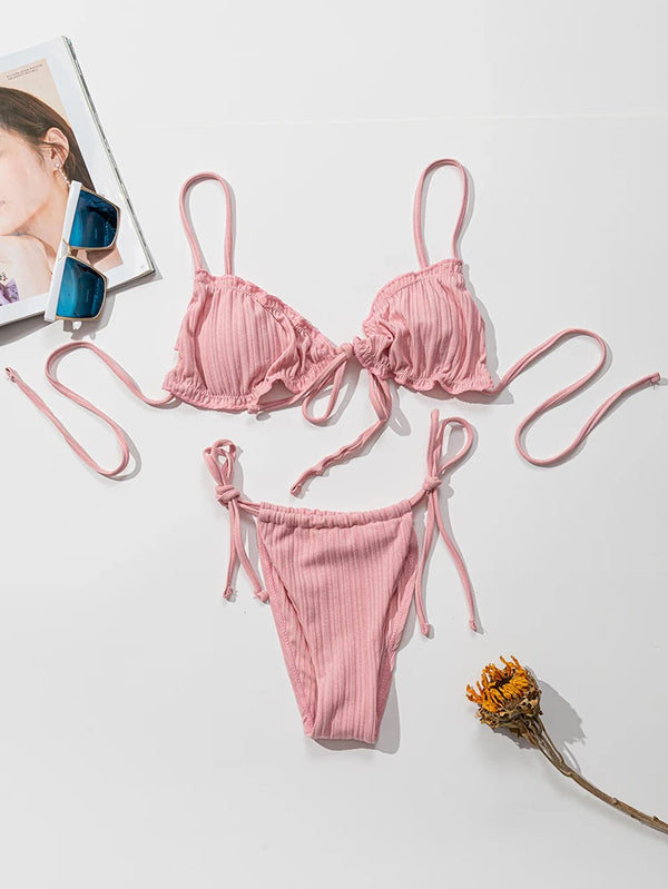 Pink bikini set on a white surface with a magazine and sunglasses.