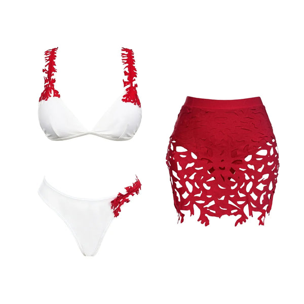 White bikini top with red floral details and a matching white bottom, alongside a red lace skirt on a white background.