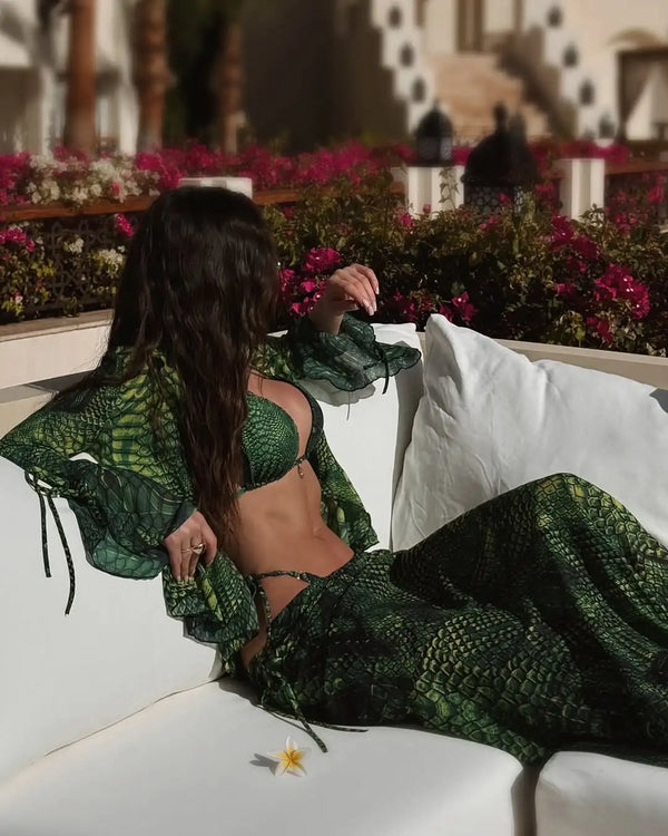 Woman in a green patterned outfit sitting on a white couch with flowers in the background