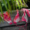 Pink and white bikini set with watermelon print on a wooden surface with green leaves in the background