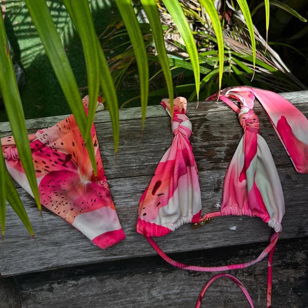Pink and white bikini set with watermelon print on a wooden surface with green leaves in the background