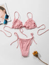 Pink bikini set on a white surface with a magazine and sunglasses.