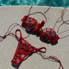 Red bikini with floral embroidery on a concrete surface near a pool.