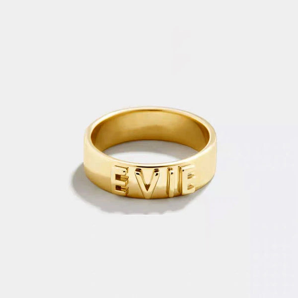 Gold ring with 'EVIE' engraving on a light gray background