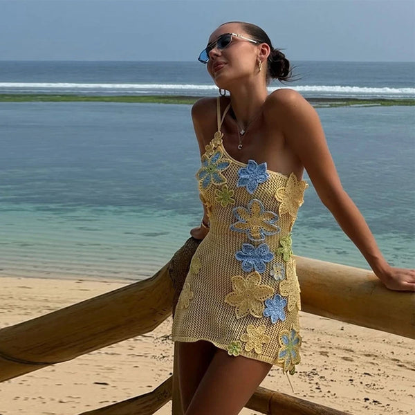 Woman in a floral crochet dress standing on a beach with ocean in the background