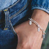 Silver anklet with name tags on a person's ankle wearing blue jeans.