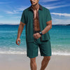 Man wearing a green shirt and shorts set on a beach with blue ocean and sky.