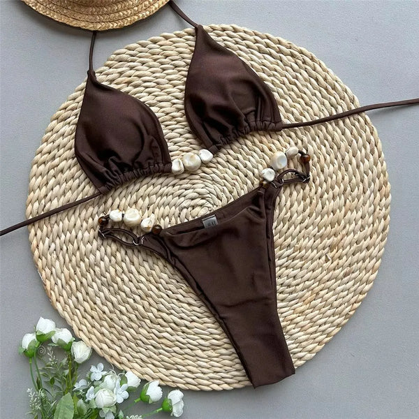 Brown bikini set with pearl details on a woven mat with flowers.