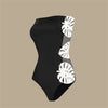 Black swimsuit with white leaf patterns on a beige background