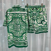 Green and white patterned shirt and shorts set on a hanger against a light curtain background.