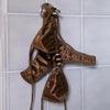 Brown satin thong hanging on a hook against a tiled wall.
