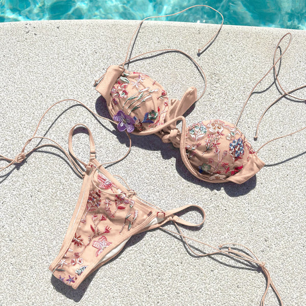 Floral embroidered bikini set on a concrete surface near a pool.