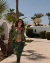 Woman in green outfit walking in a palm tree-lined area with white buildings.