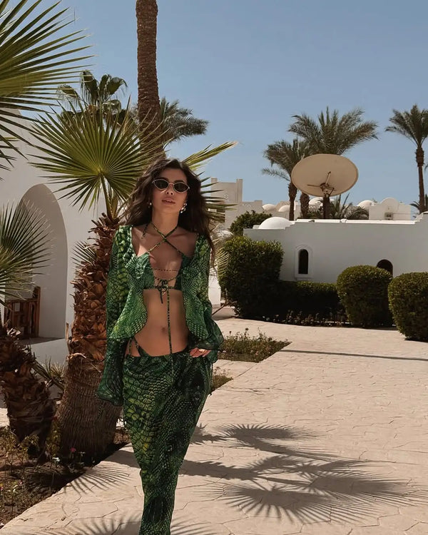 Woman in green outfit walking in a palm tree-lined area with white buildings.