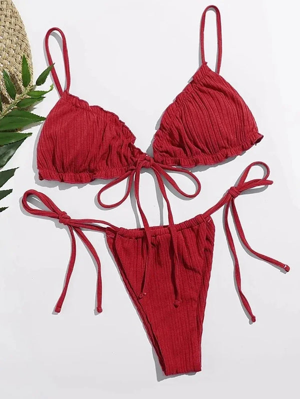 Red bikini set on a white background with a straw hat and green leaves.