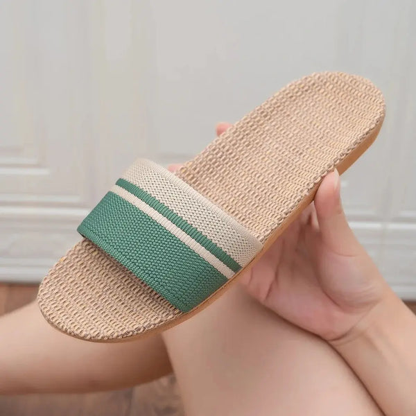 Beige slide sandal with green and white strap held by a hand against a neutral background