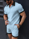 Man wearing a light blue textured shirt and shorts with black trim against a dark background