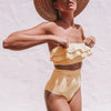 Woman wearing a yellow and white striped bikini with a wide-brimmed hat on a light background