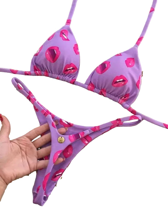 Purple bikini set with pink lip prints on a decorative mat, brand tag visible.