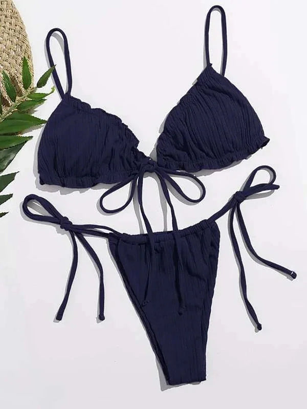 Navy blue bikini set on a white background with a straw hat and green leaves.