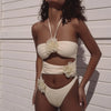 Woman wearing a white bikini with floral details against a light-colored wall.