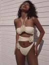 Woman wearing a white bikini with floral details against a light-colored wall.