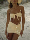Woman wearing a beige bikini with pom-pom details on a sandy beach.